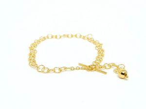 Feines, goldenes Armband mit runden Ösen und einem Knebelverschluss. Das Armband liegt auf weißem Untergrund.