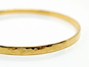 Geschmiedeter, goldener Armreif, der auf weißem Untergrund liegt.